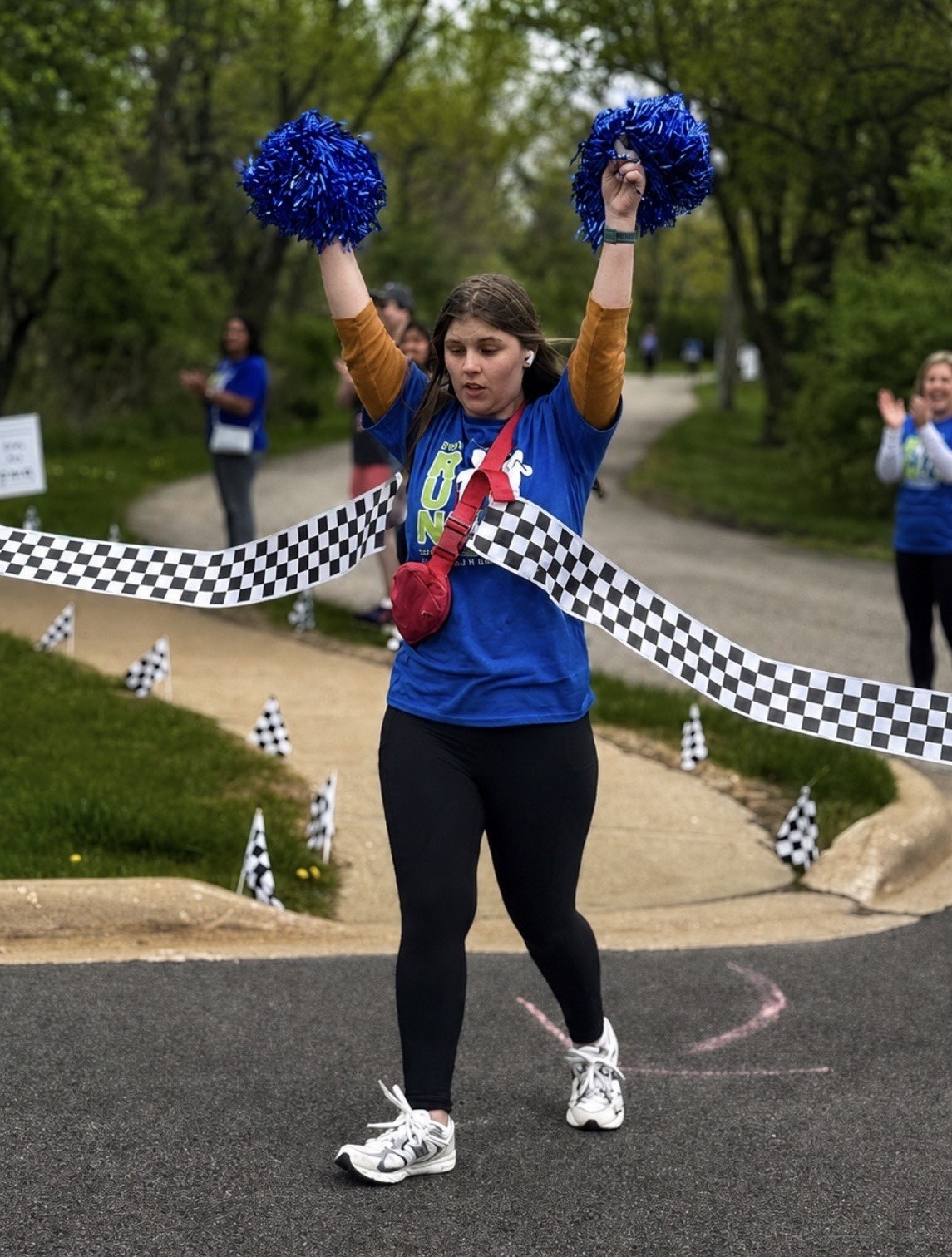 A Soaring Eagle Academy student crosses the finish line at the annual Fun Run & Roll, blue pom-poms raised.